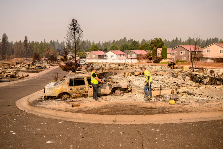 A row of homes stands behind the debris remaining of blocks of houses that burned.