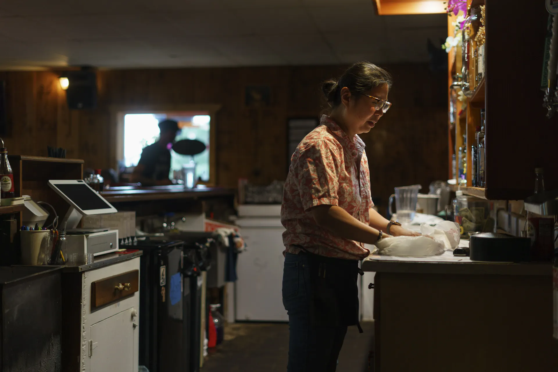 A woman in a small commercial kitchen preps a takeout order.