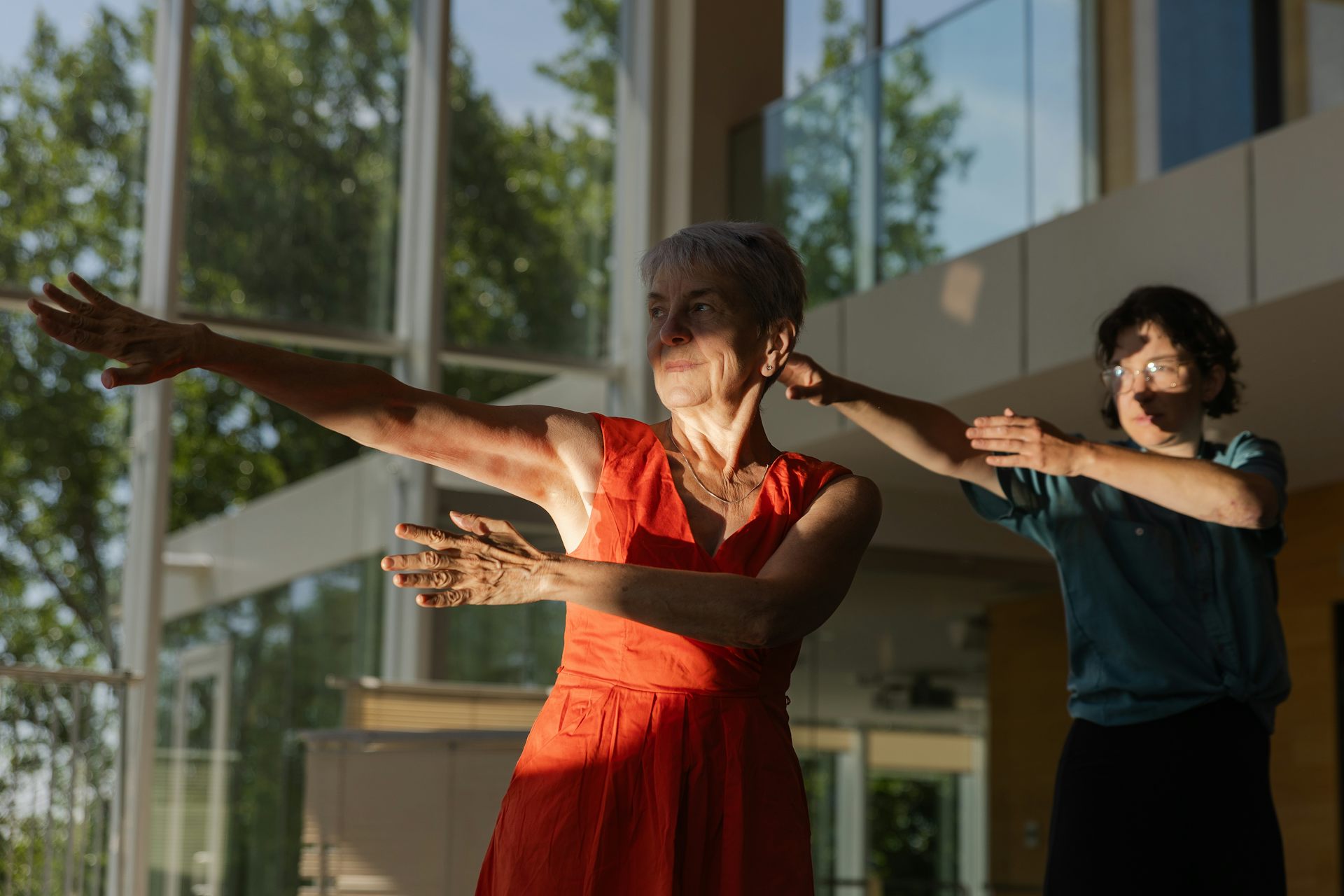 Two people stand with their arms pointed to the left of the picture at shoulder level, lit by a stripe of sunlight.