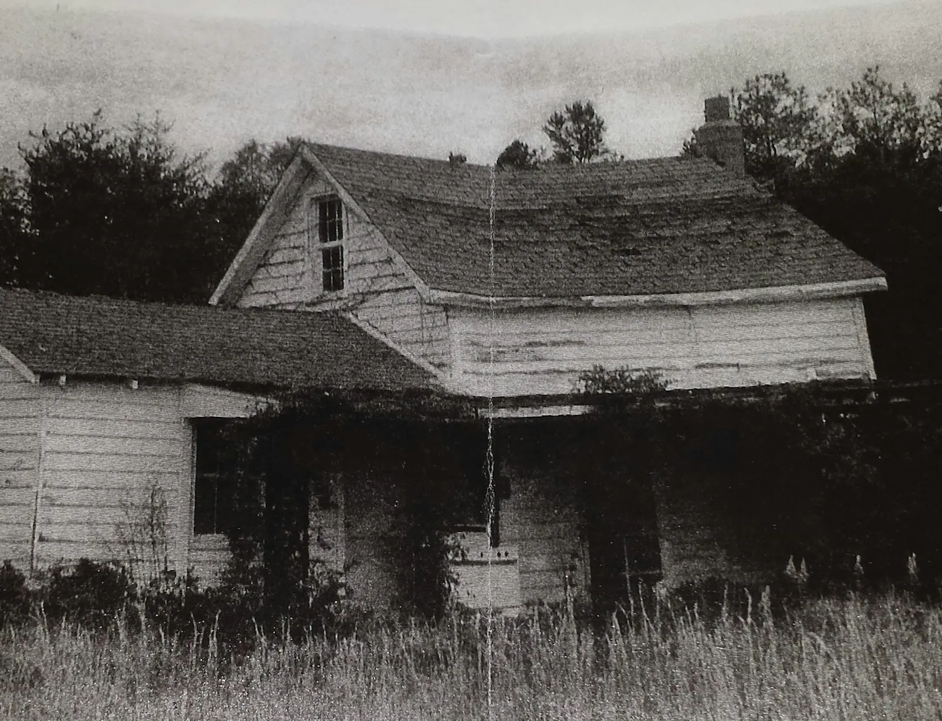 A black-and-white photo of a two-story white house with a one-story section on one end.