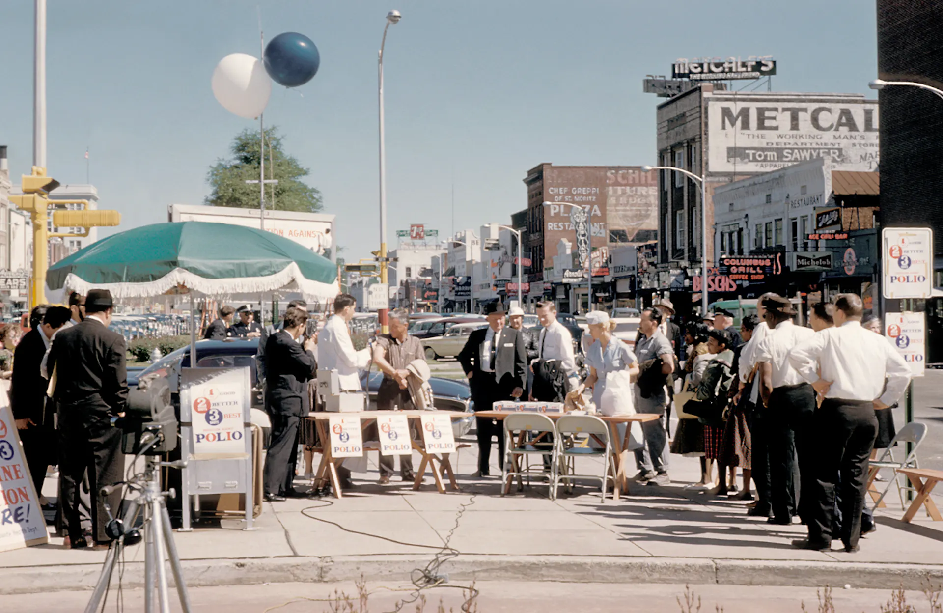 Healthcare workers standing in front of folding tables on a sidewalk give people injections.