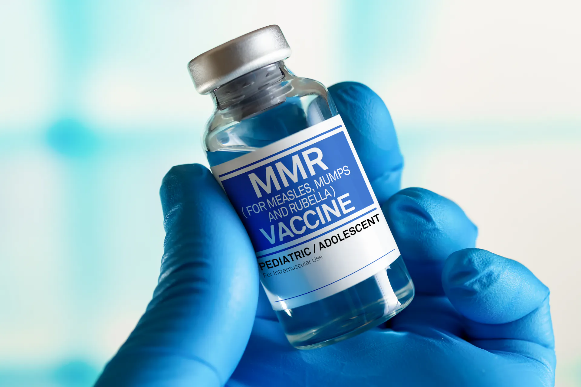 A gloved hand holding a bottle of MMR vaccine