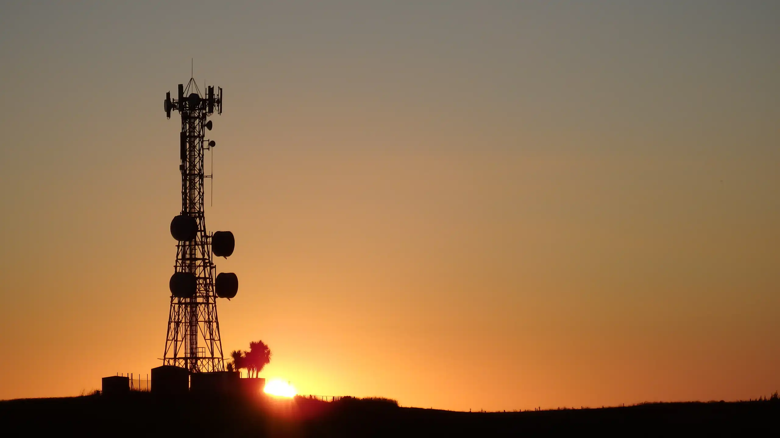 Un pylône de télécommunications devant un soleil couchant.