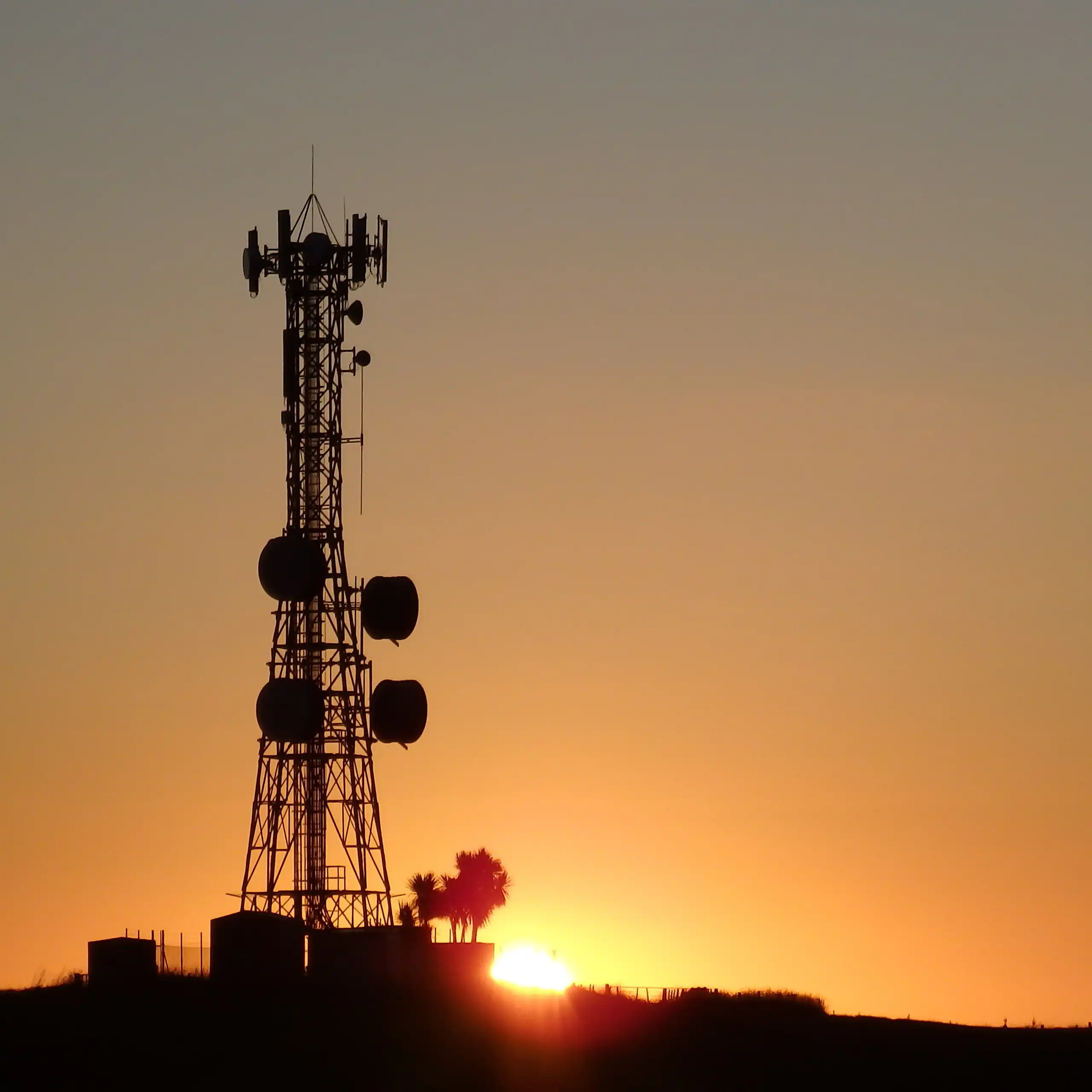 Un pylône de télécommunications devant un soleil couchant.