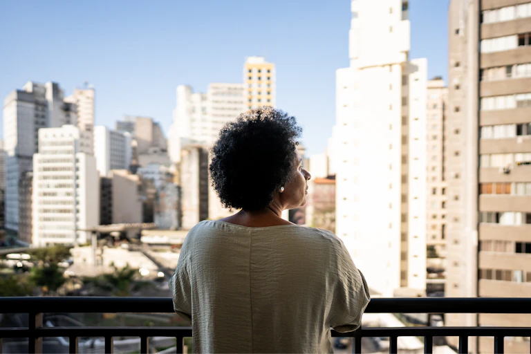 Older woman looks from balcony over city.