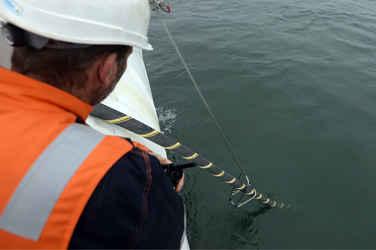 A worker in high visibility clothing on a boat inspecting a subsea cable.