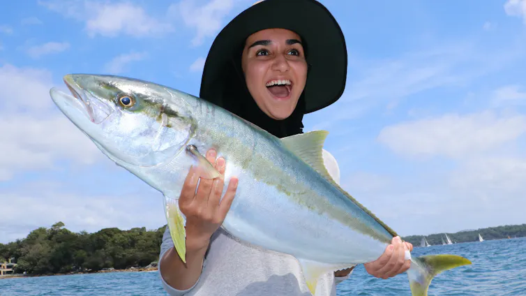 A woman holds up a yellowtail kingfish.