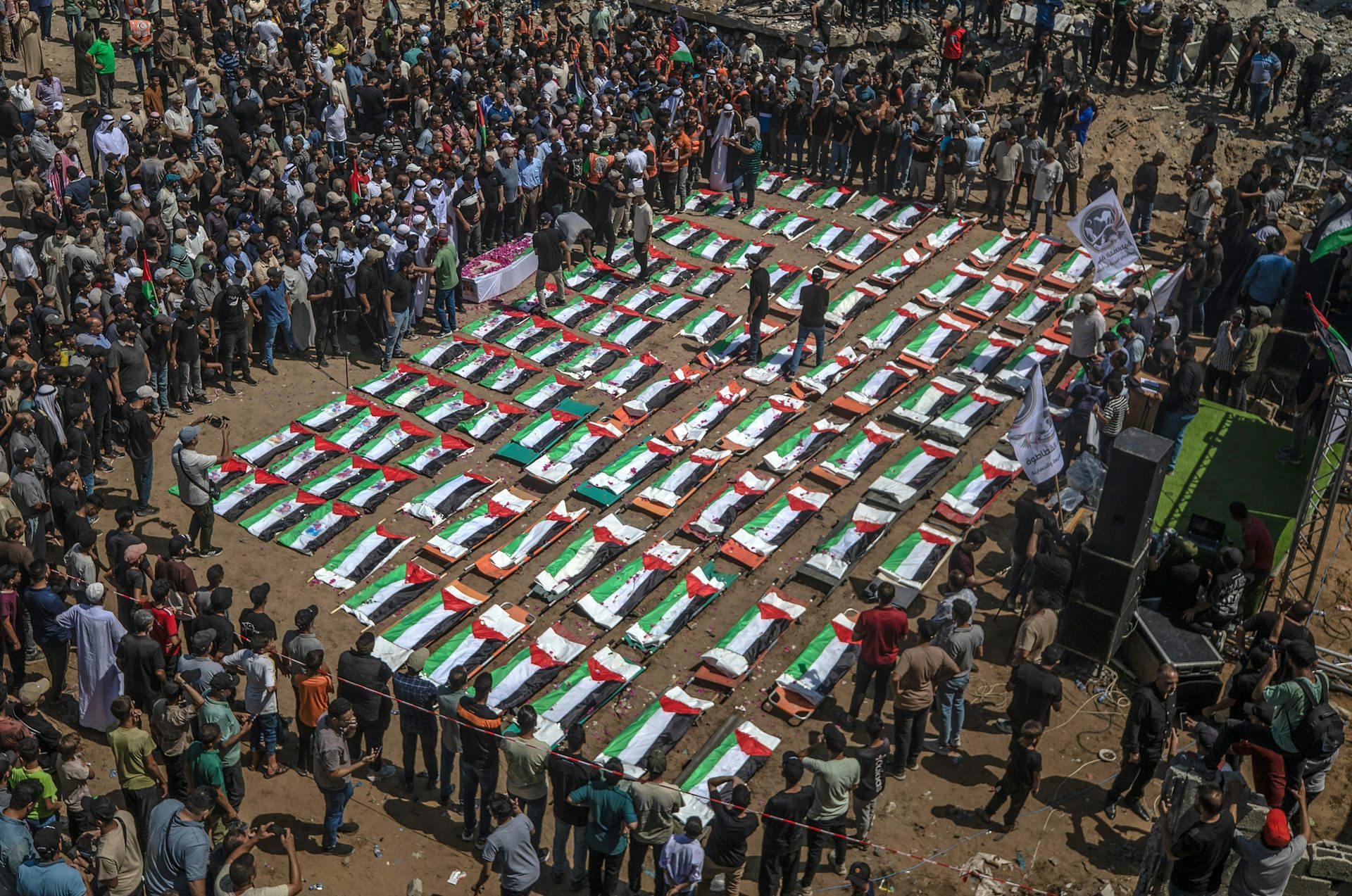 A large crowd of people around the coffins of 112 people which are wrapped in Palestinian flags.