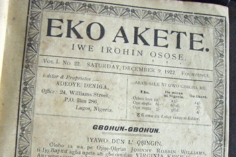 A black and white photo of a vintage newspaper with an ornate border, printed words and the title 'Eko Akete'.