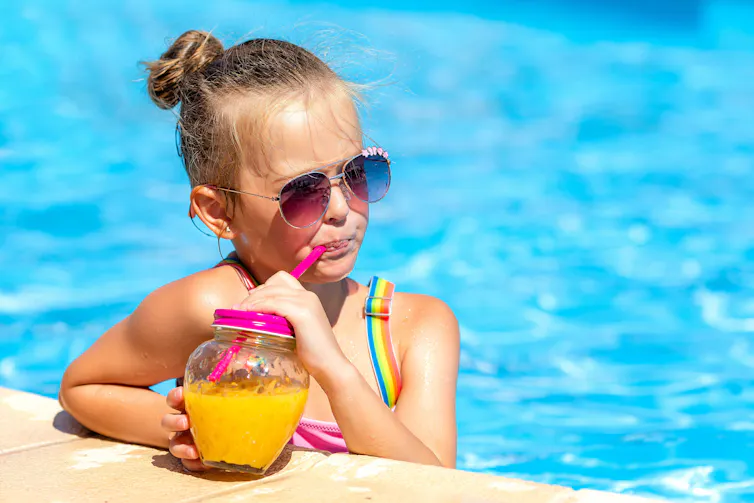 Little girl holding fresh cocktail at swim up cafe