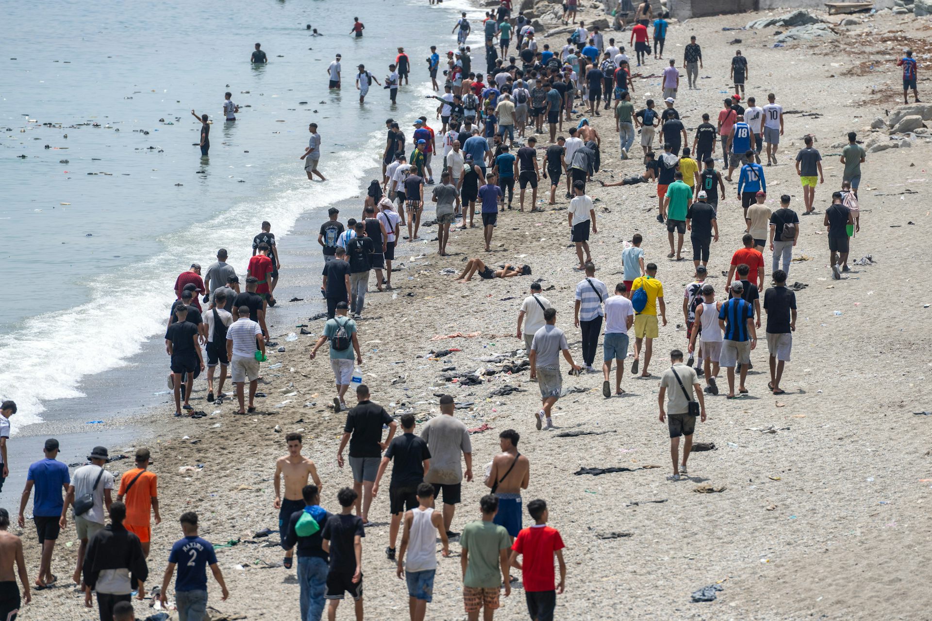 A crowd of people walk along a beach.