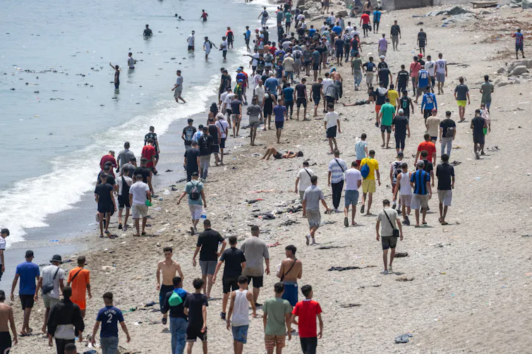 A crowd of people walk along a beach.