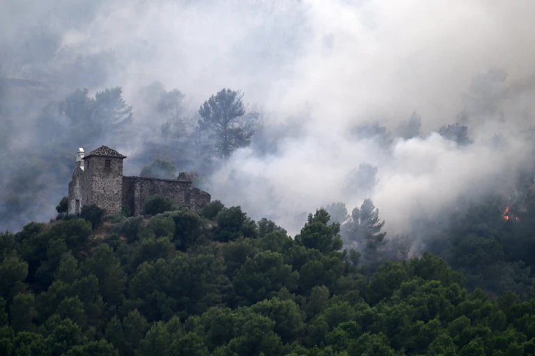 A stone chapel on a hillside with wildfire smoke around it.
