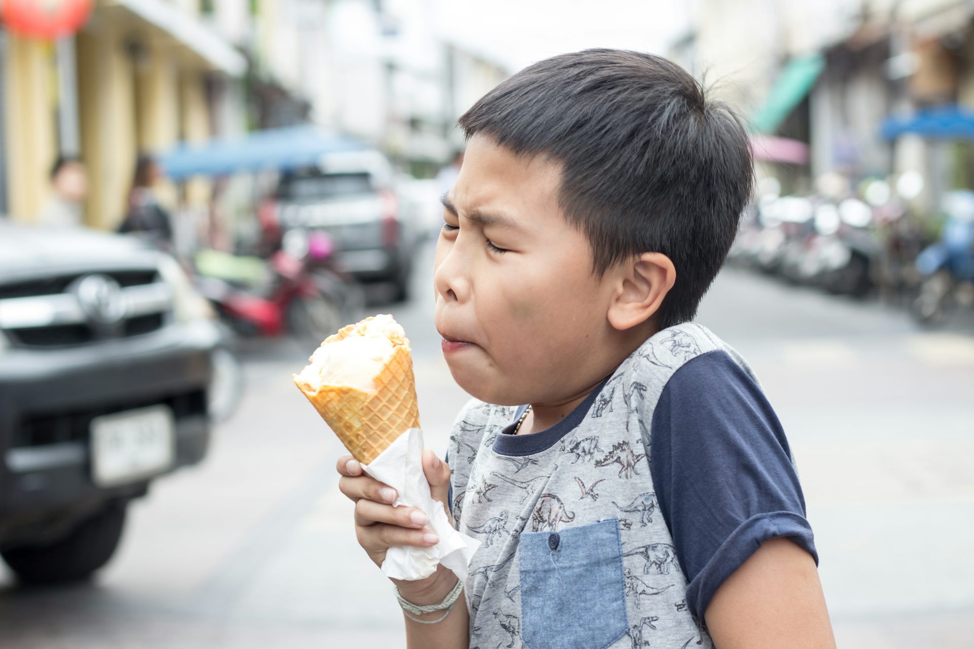 Young boy winces due to pain from brain freeze while holding an ice cream.