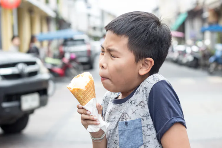 Young boy winces due to pain from brain freeze while holding an ice cream.