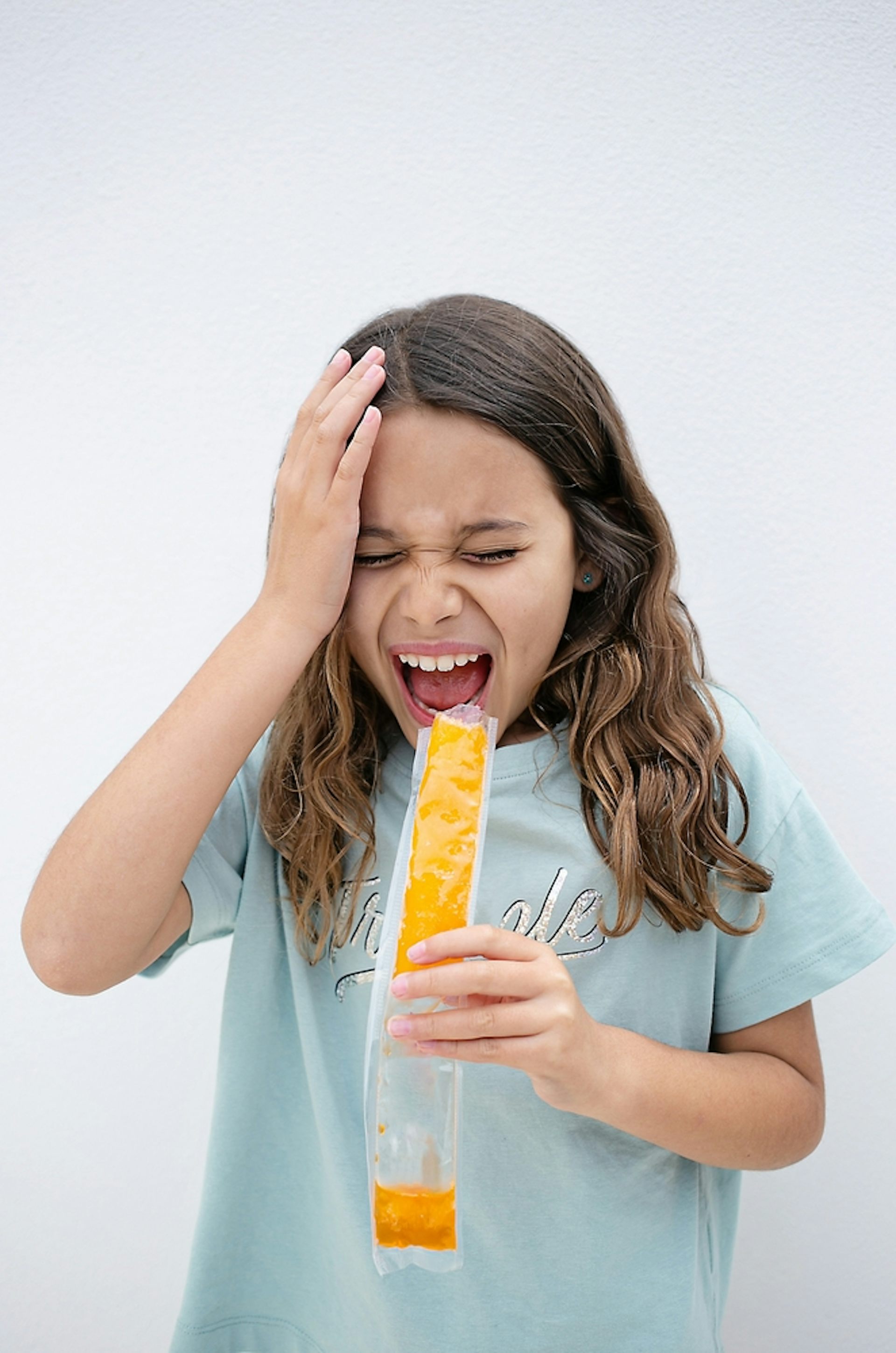Young girl eating an iced lolly holds her head and screams in pain