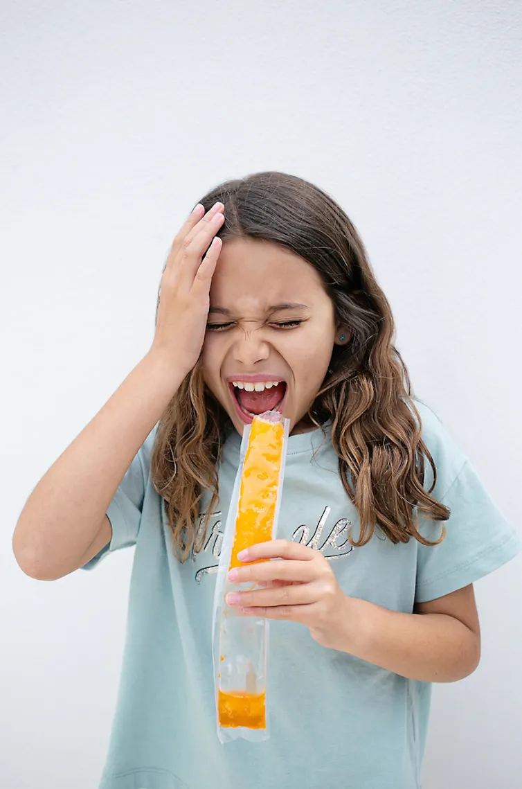 Young girl eating an iced lolly holds her head and screams in pain
