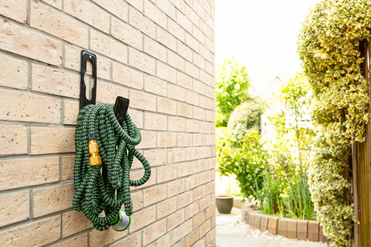 hosepipe on brick wall, garden in background