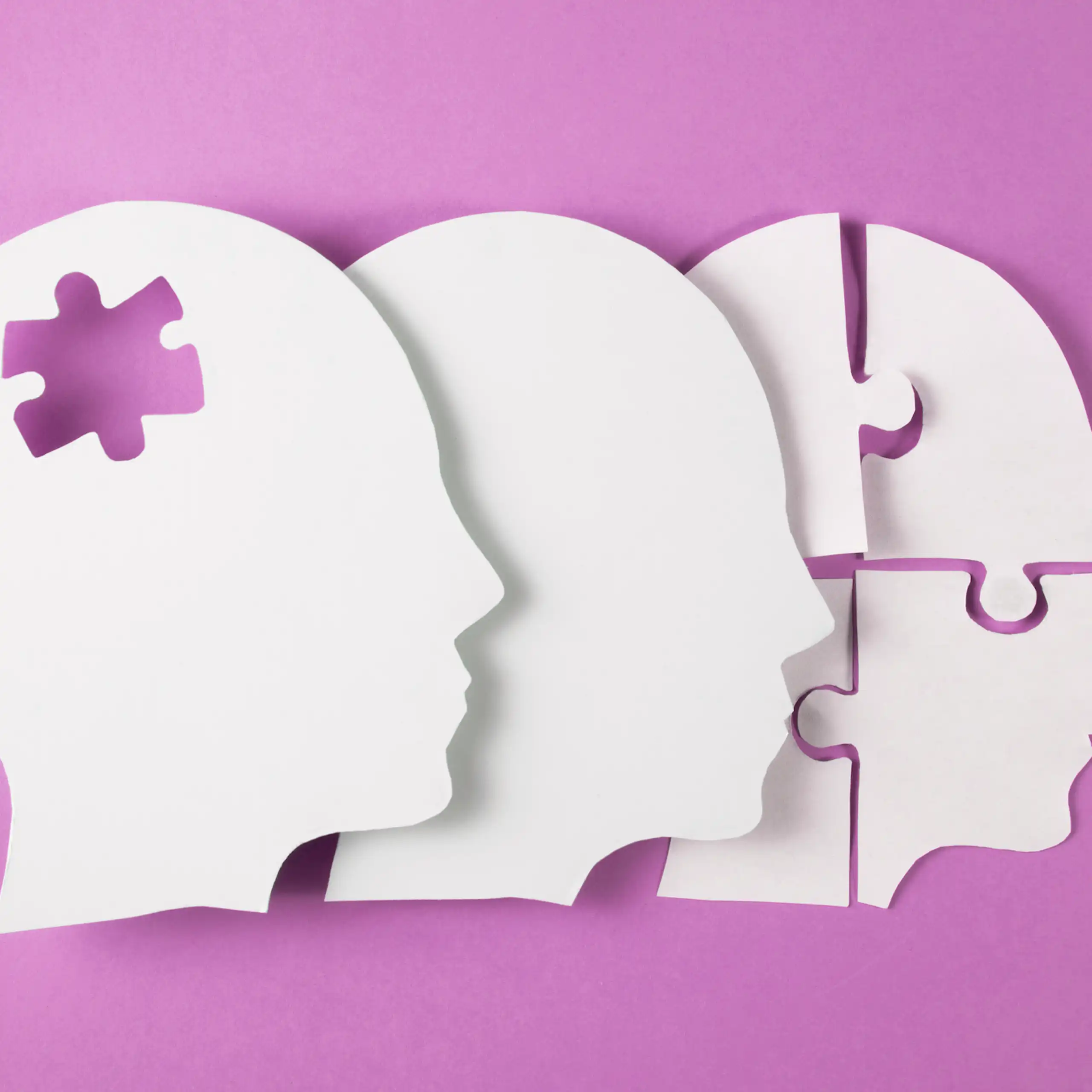 Illustration of white silhouettes of three overlapping side profiles, one missing a puzzle piece in its head and one split into four puzzle pieces