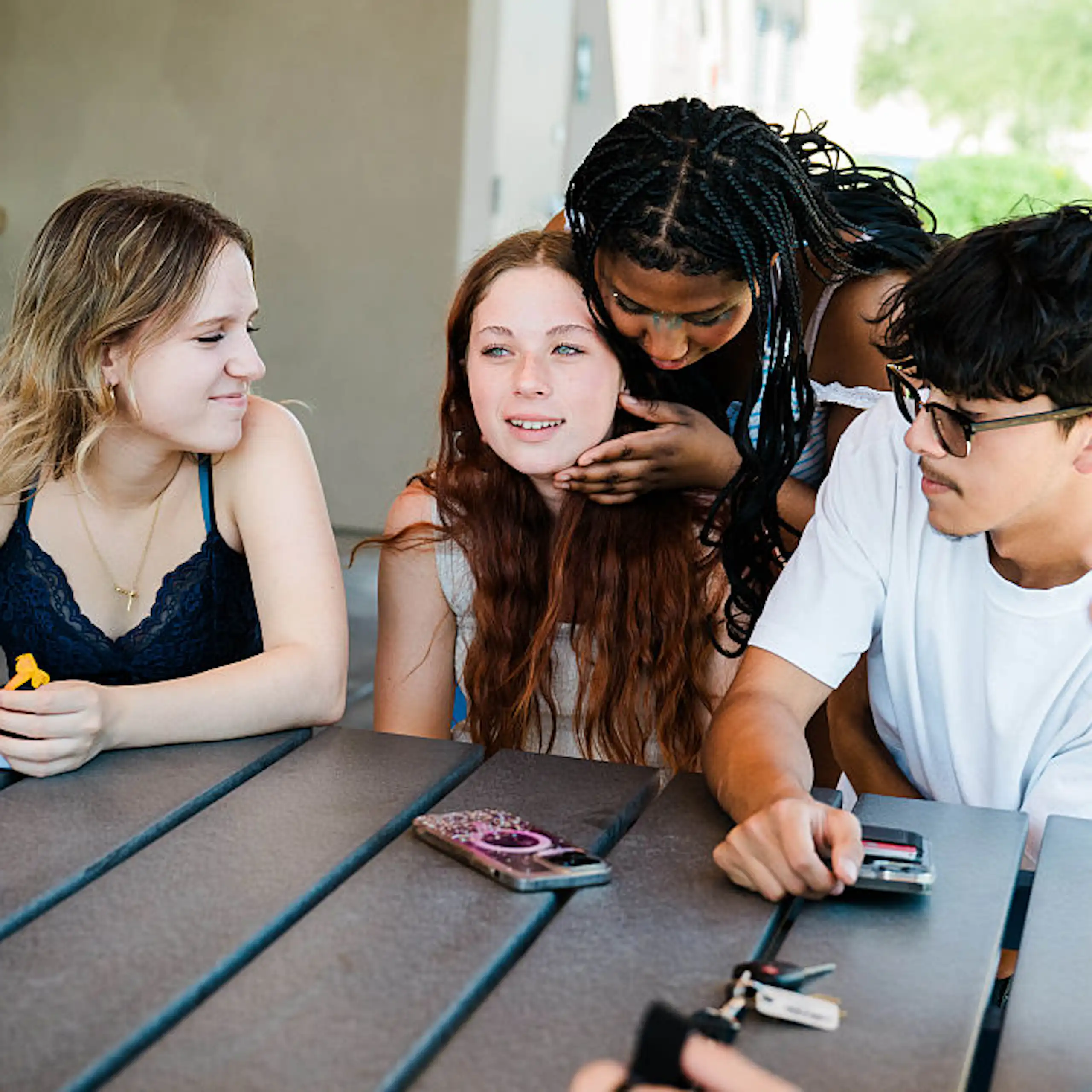 A group of teenagers sit around a table outside.