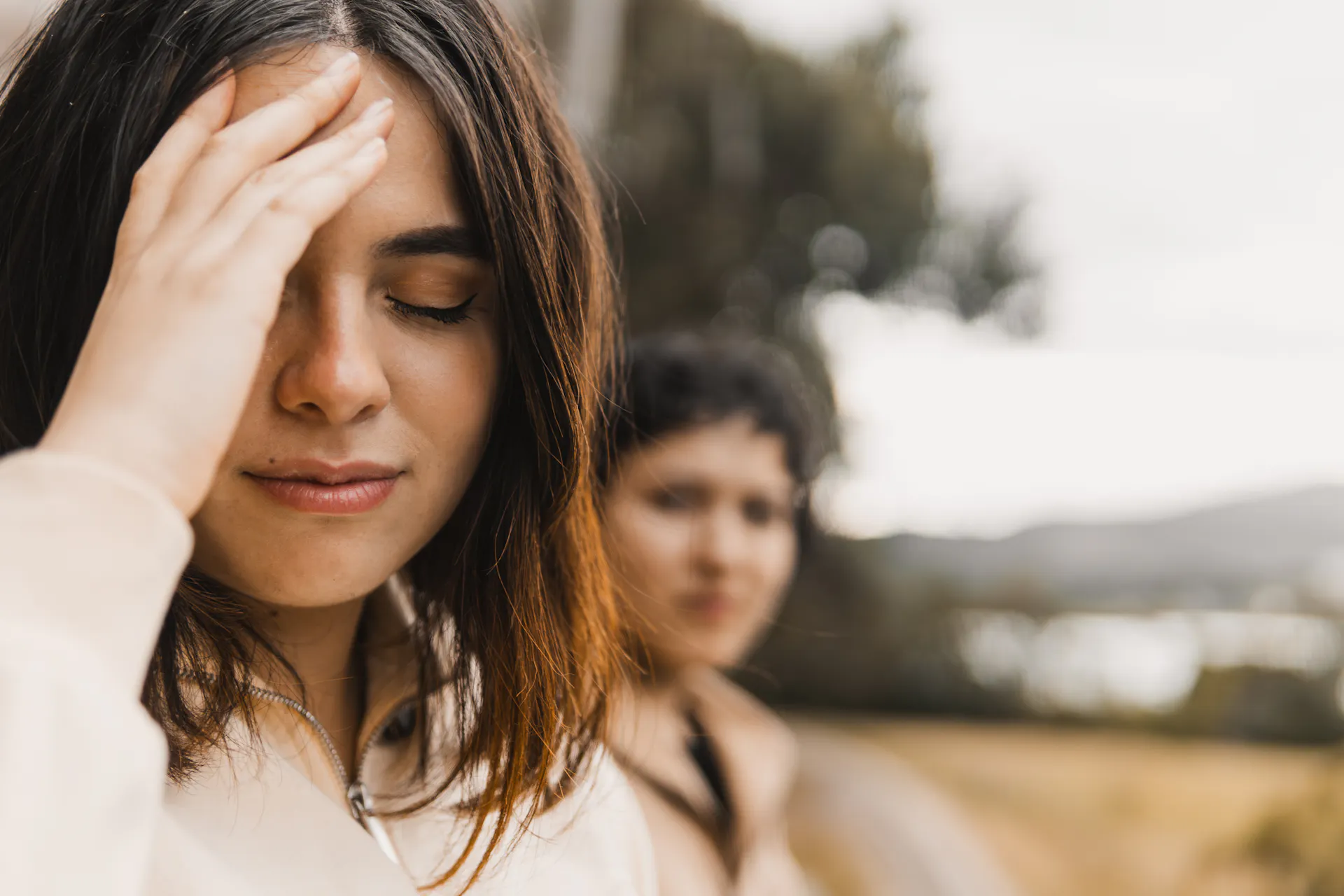 Person turned away from another person, hand pressed to their forehead with closed eyes