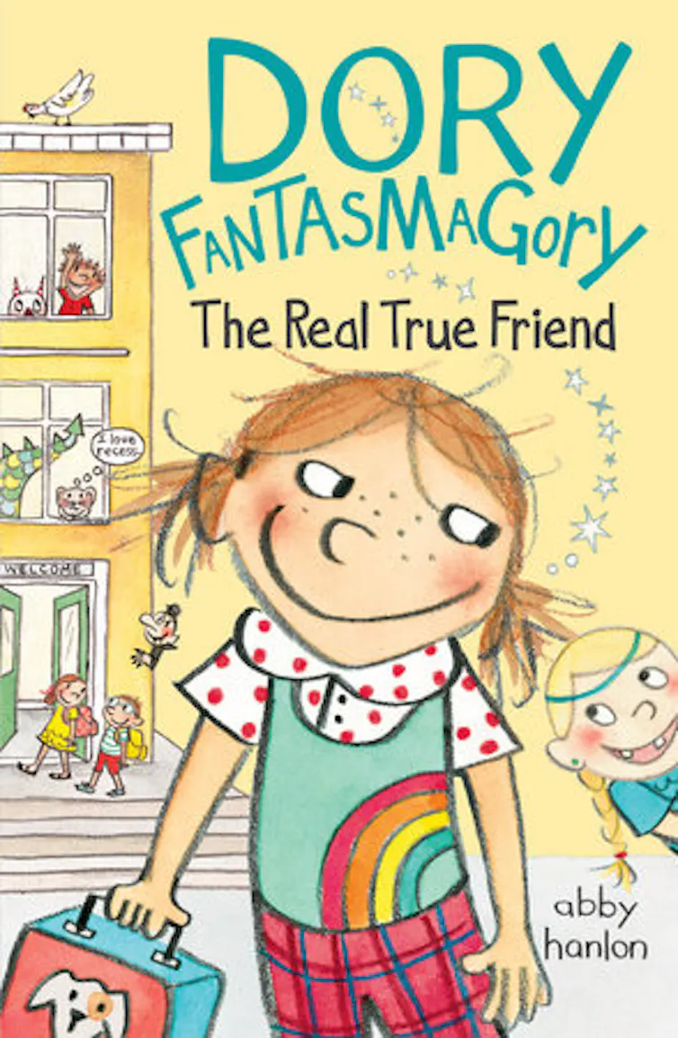 Une couverture de livre jaune pâle indique « Dory Fantasmagory The Real True Friend » et montre une image de dessin animé d'une jeune fille vêtue d'une chemise verte avec un arc-en-ciel dessus, devant un bâtiment avec des gens et des personnages de dessins animés sortant de ses portes et fenêtres.