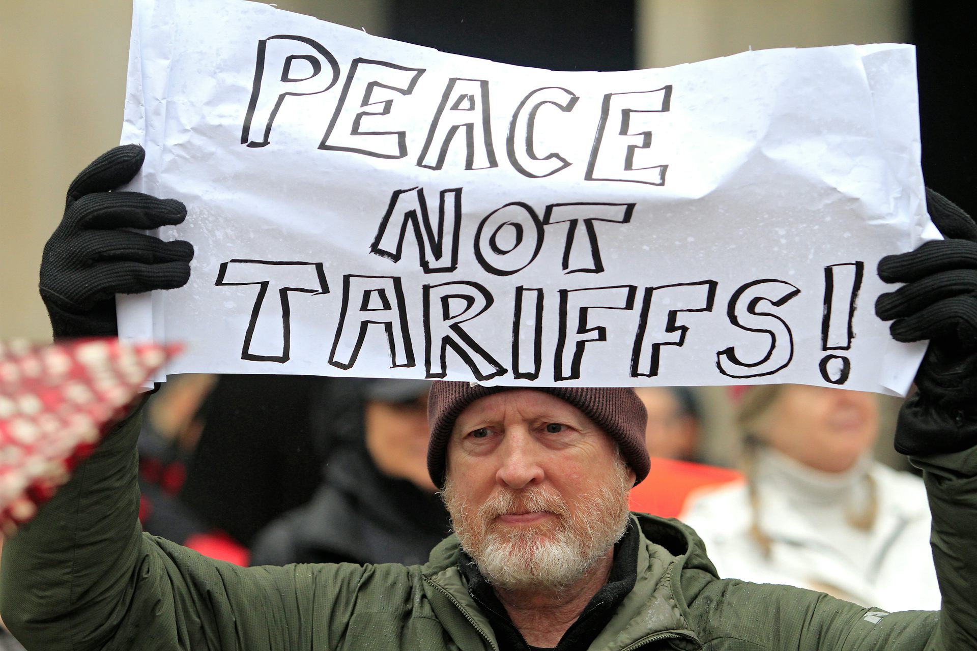 A bearded man holds up a sign, 'Peace Not Tariffs,' at an anti-Trump rally in Toronto.
