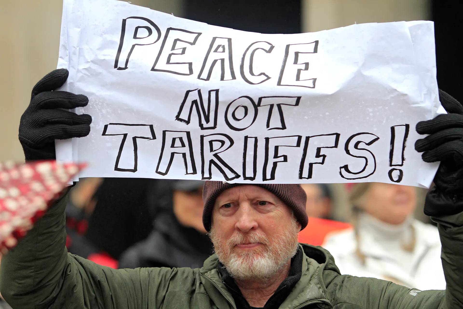 A bearded man holds up a sign, 'Peace Not Tariffs,' at an anti-Trump rally in Toronto.