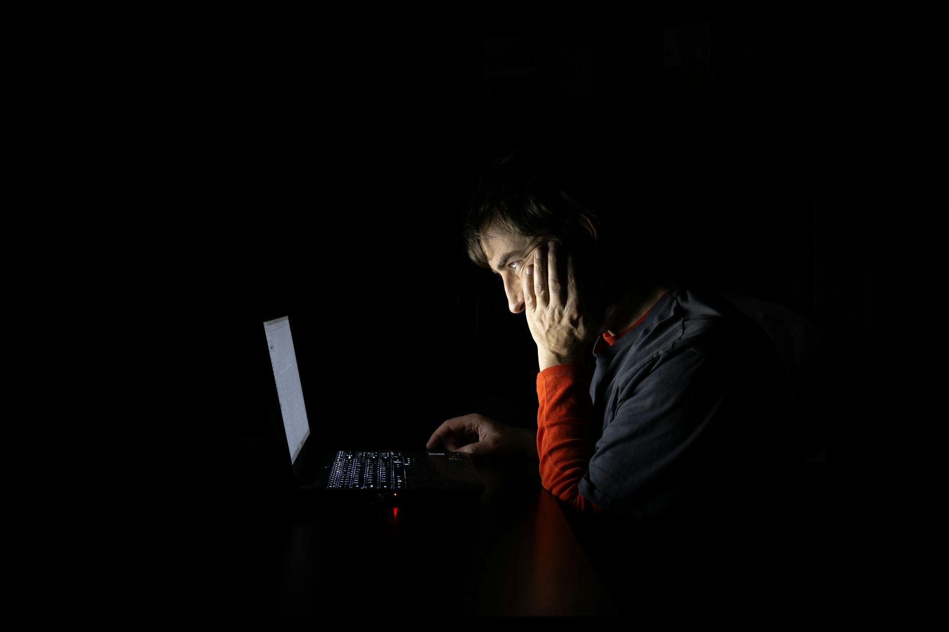 Um jovem, na penumbra, olha para a tela de um laptop