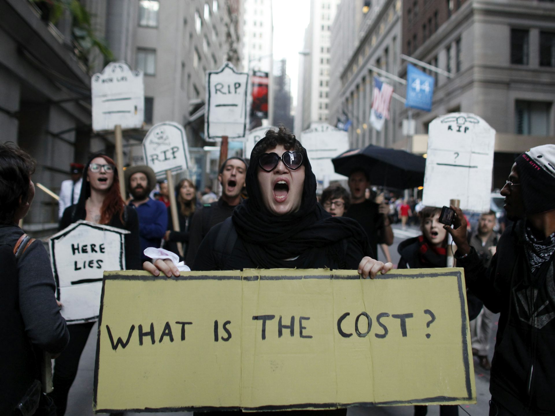 Young protestors chant during an Occupy Wall Street march, with one sign reading: 'WHAT IS THE COST?'