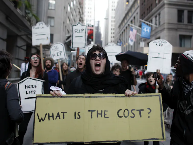 Young protestors chant during an Occupy Wall Street march, with one sign reading: 'WHAT IS THE COST?'