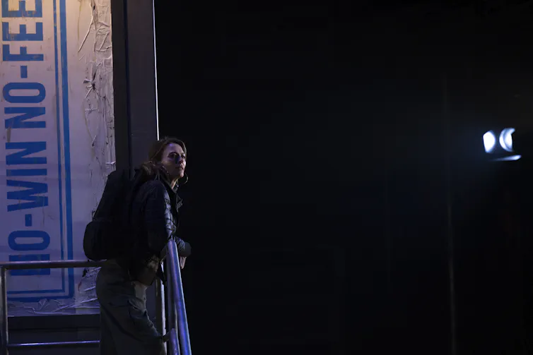 Production image: Pamela stands at the top of some stairs.