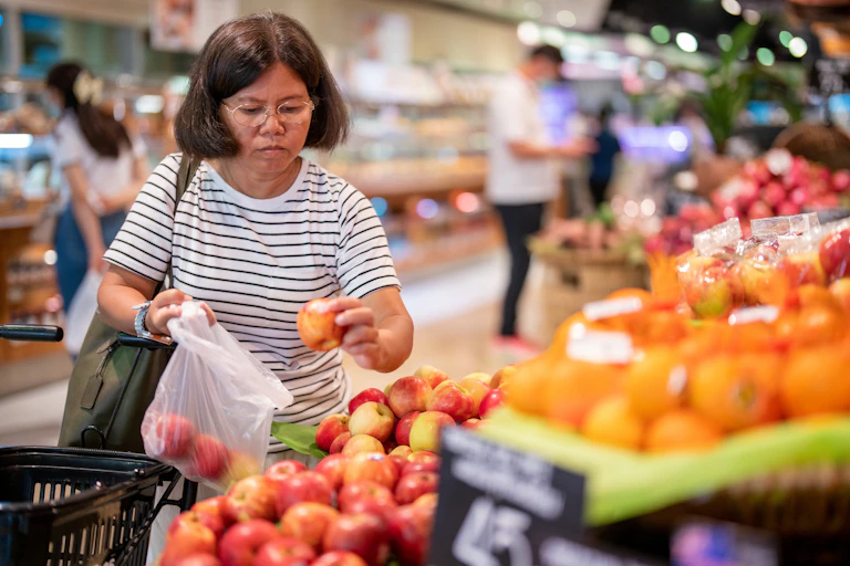 Middle-aged woman chooses apples at a grocery store.