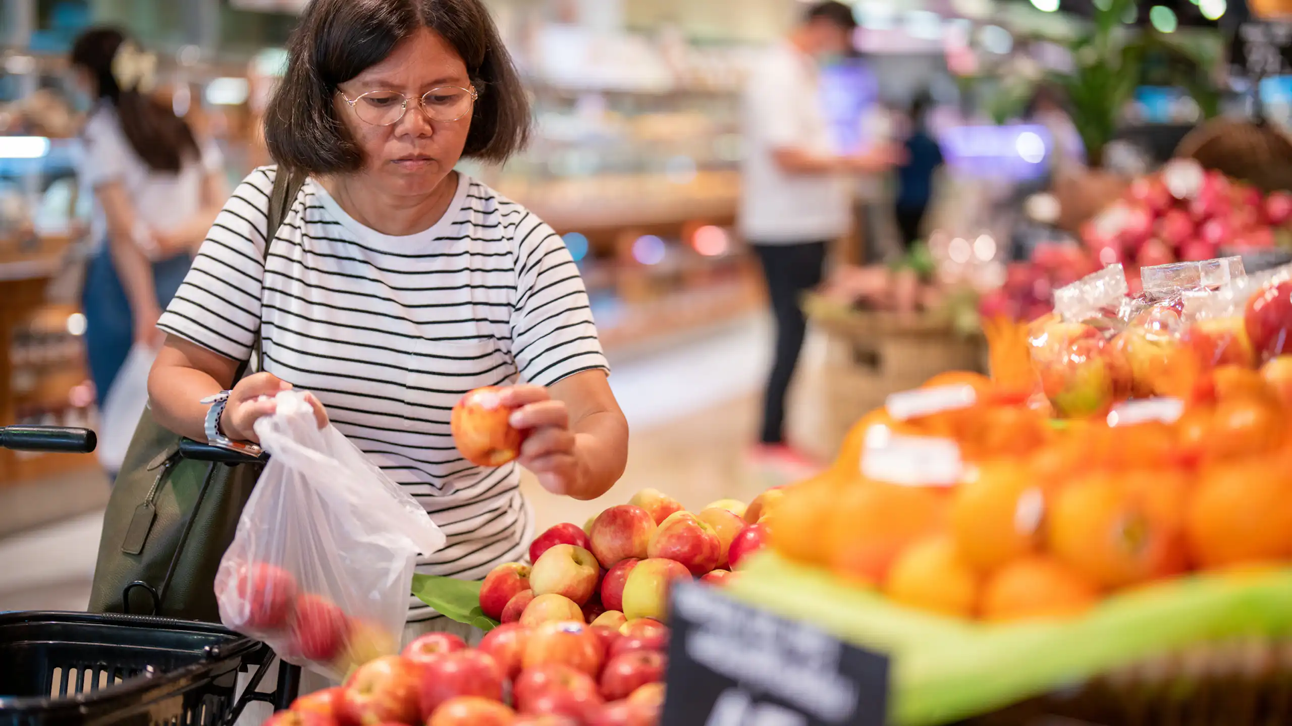 Middle-aged woman chooses apples at a grocery store.