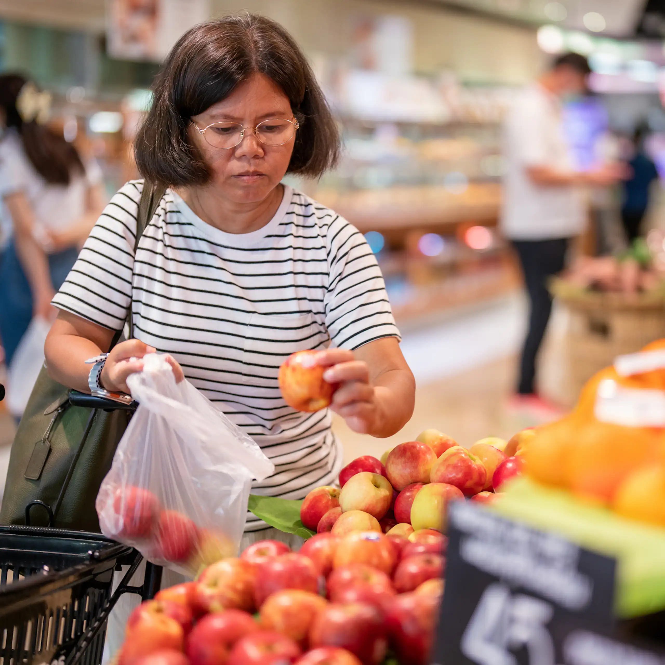 Middle-aged woman chooses apples at a grocery store.