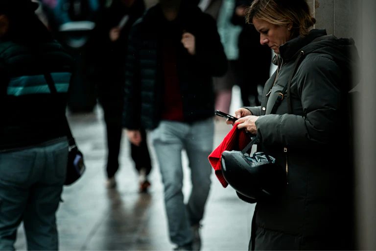 A woman leans up against a wall on a public street and scrolls on her smartphone