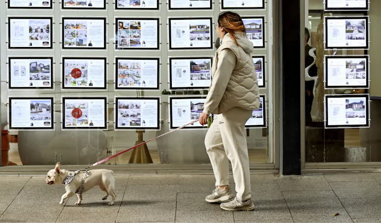 A woman and her dog walk past a real estate agency's display in Melbourne.