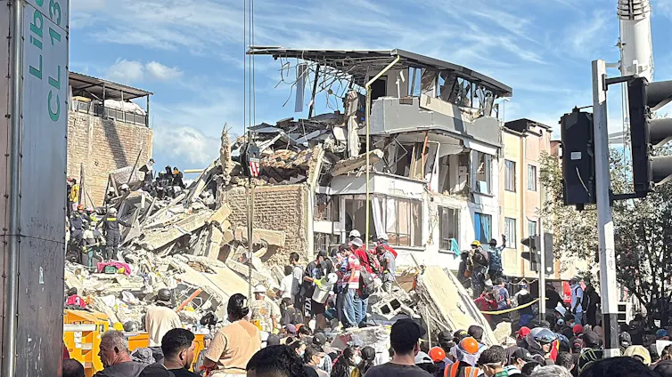 Edificio destruido por el terremoto, personas mirando y profesionales trabajando sobre los escombros