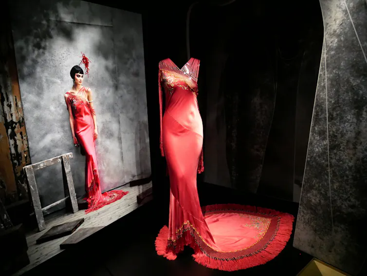 Vestido rojo de estilo flamenca de alta costura de John Galliano exhibido en París en la Galería Dior. Hay una reproducción grande al fondo de una fotografía de una modelo vistiendo la prenda.