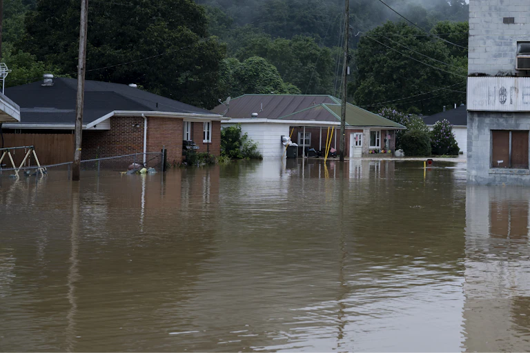 An office building and two houses partially filled with flood water with a mountain in the background.