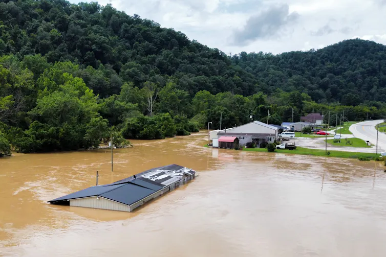 Muddy water up to the roofline of one house and at the edges of others along a river.