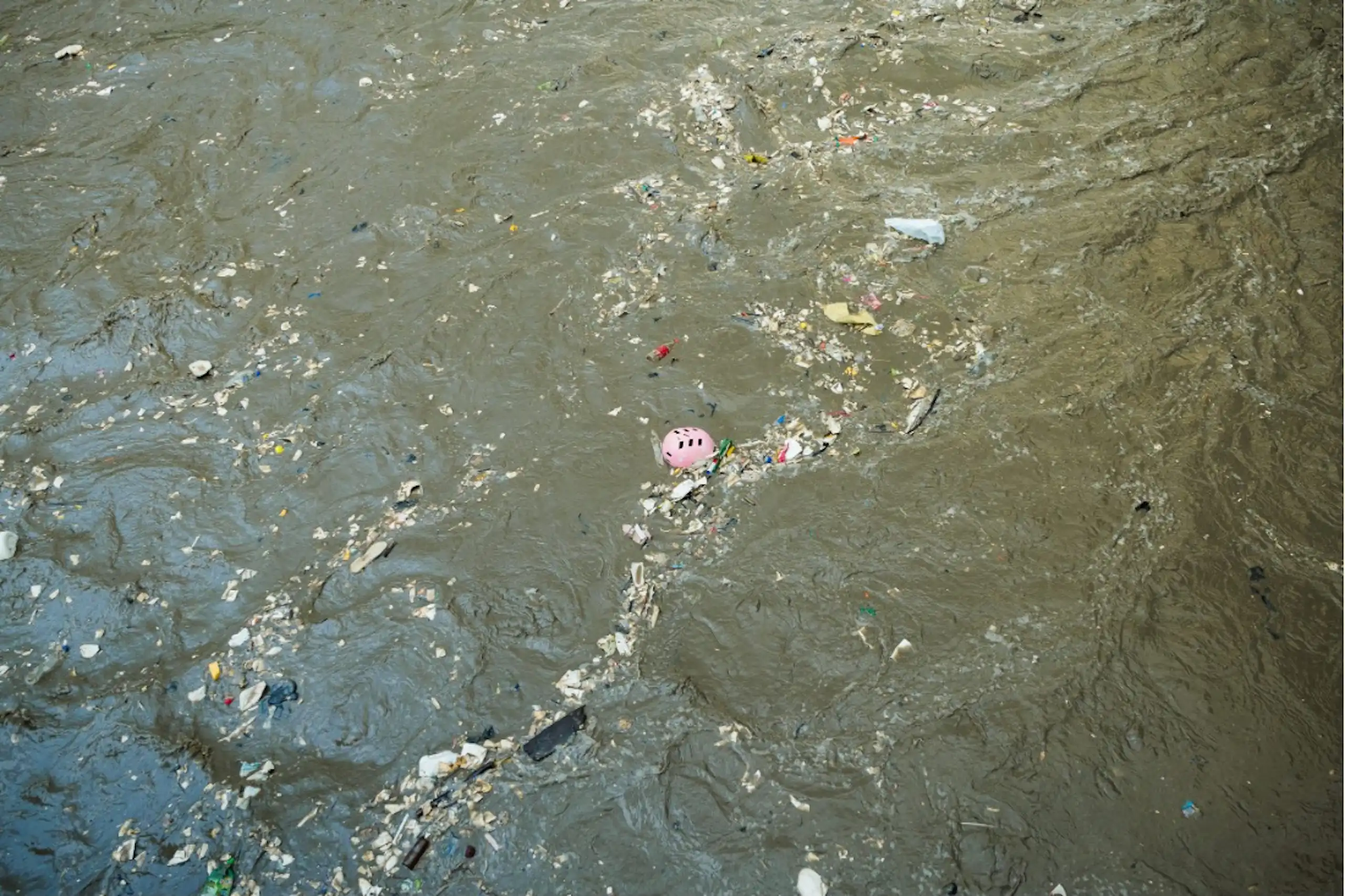 Vue de déchets plastiques (casque de vélo, bouteilles vides, emballages) flottant à la surface de l’eau.