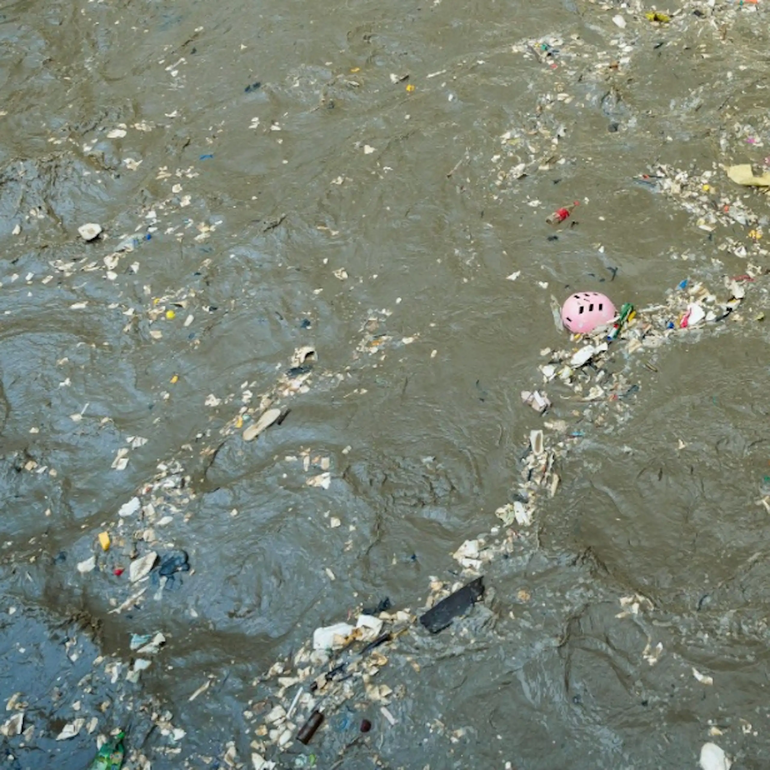 Vue de déchets plastiques (casque de vélo, bouteilles vides, emballages) flottant à la surface de l’eau.