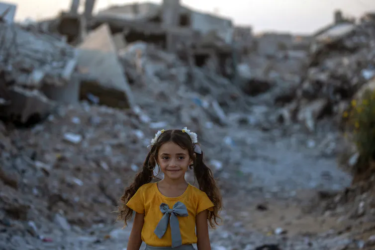 A little girl poses amid the rubble of Gaza.