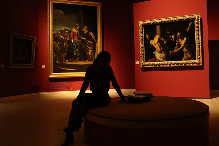 silhouette-d-une-personne-assise-sur-une-chaise-ronde dans une salle de musée aux tentures rouges