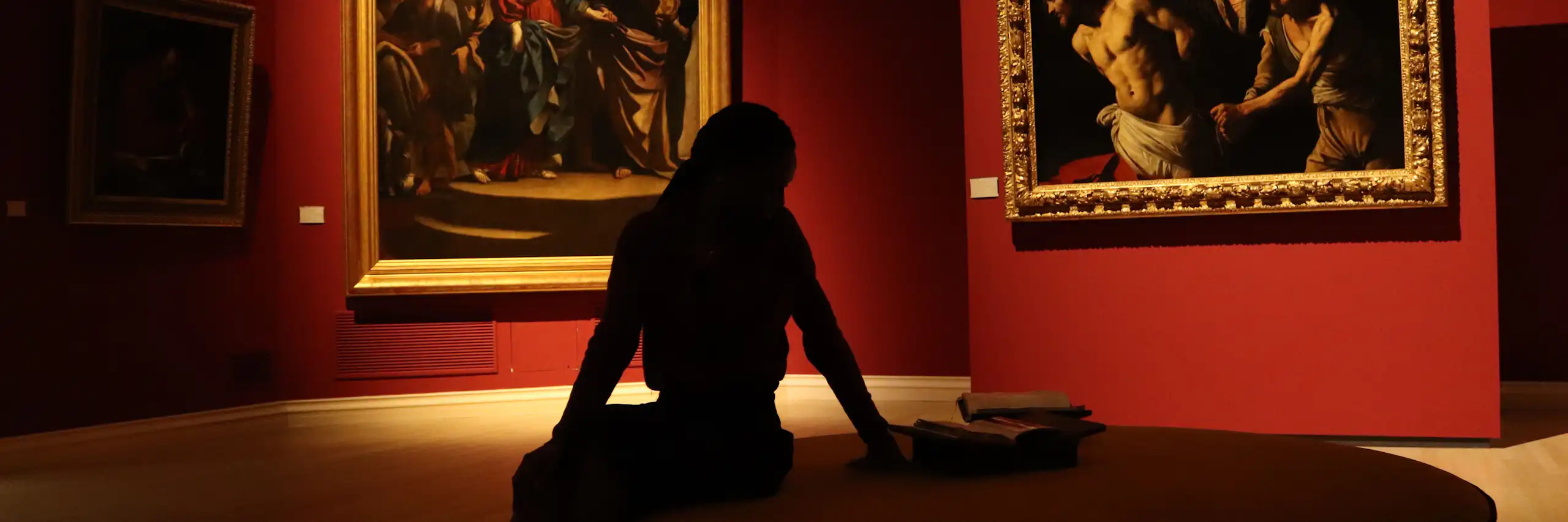 silhouette-d-une-personne-assise-sur-une-chaise-ronde dans une salle de musée aux tentures rouges