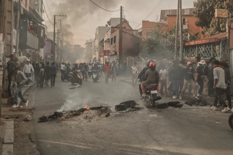 A crowd of people walking and riding on the side of a road blocked by a row of tyres that had been set alight