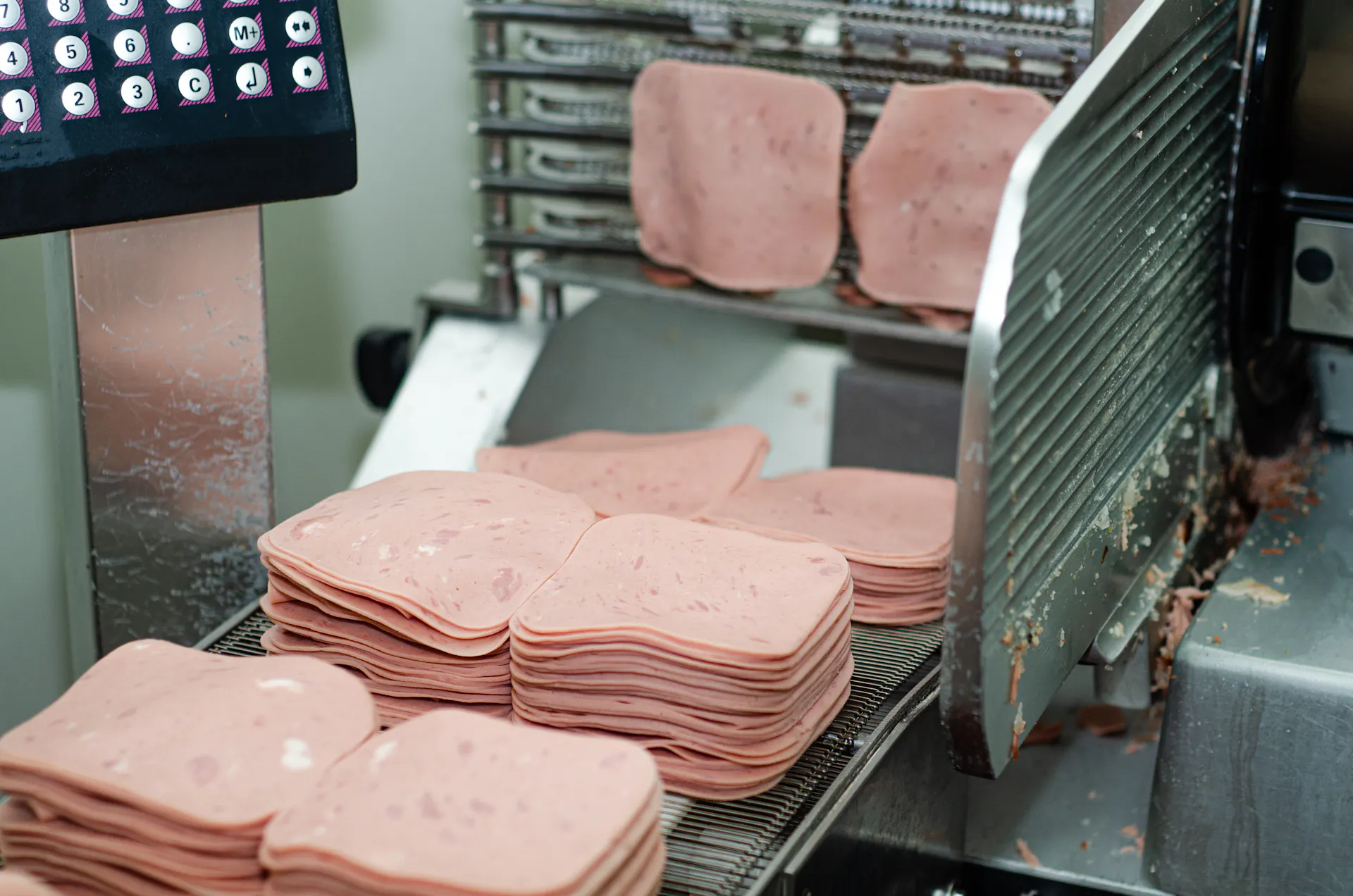 Pink lunchmeat moves through an industrial metal slicer.