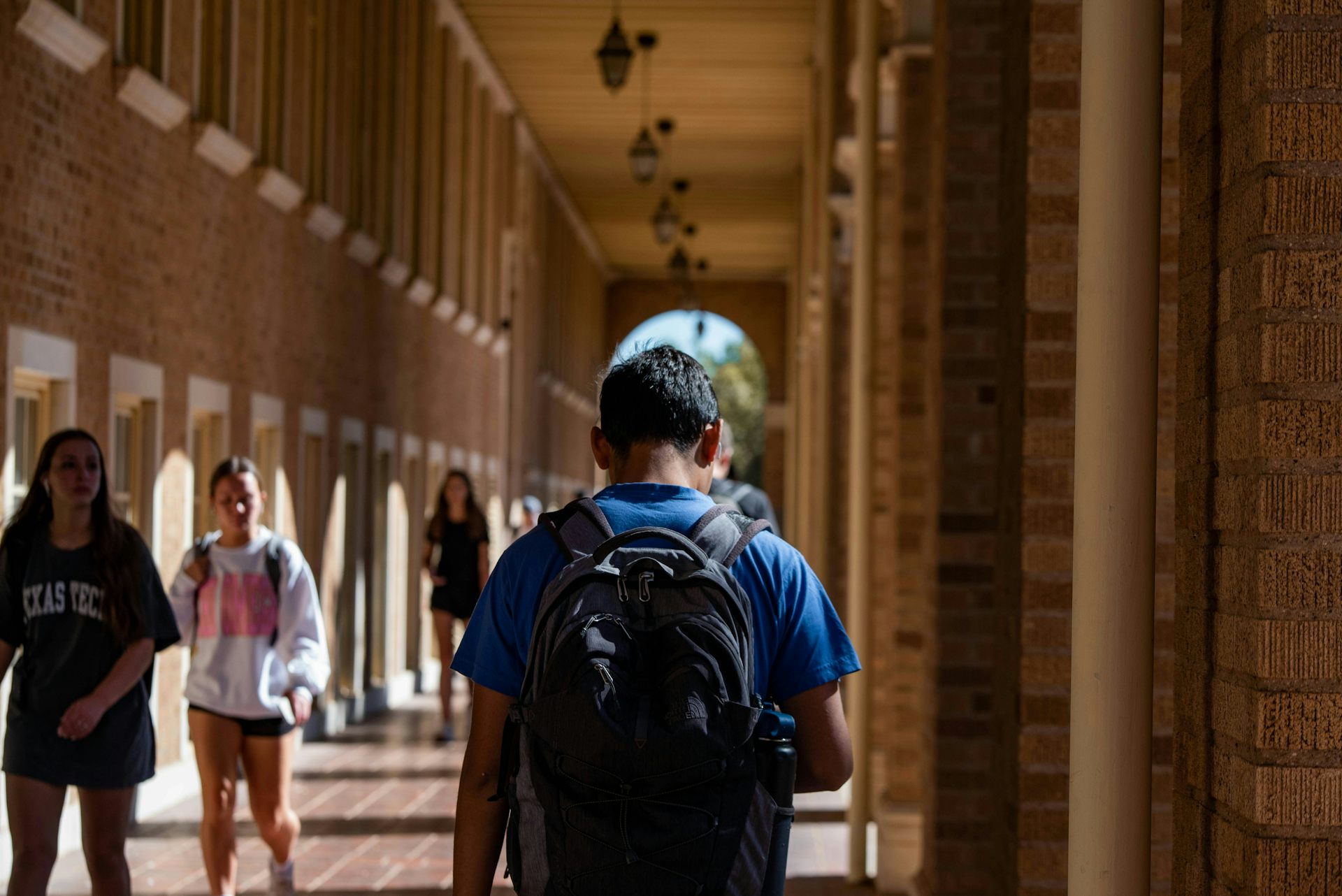 A person wearing a backpack seen from behind with two young women walking toward him in casual clothes