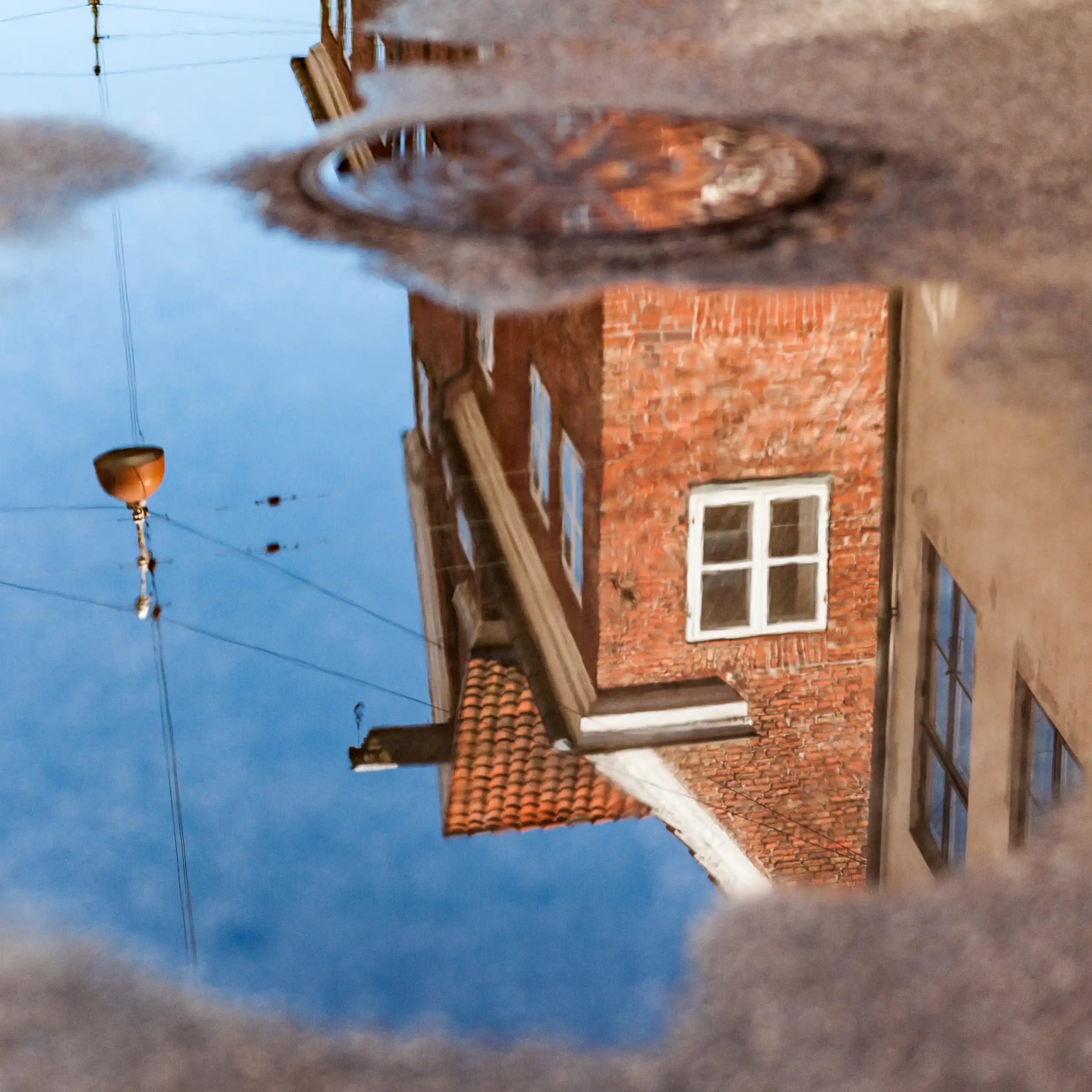 The reflection of a brick house is seen in a small puddle on the road.